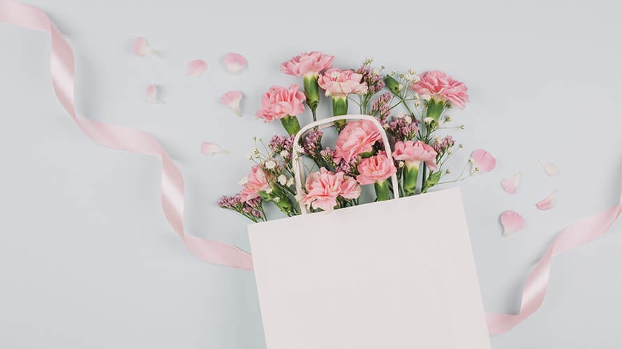 白い紙袋に入ったピンク色のカーネーションの花束